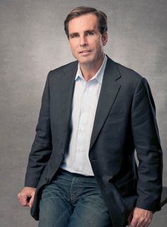 a man in a suit and jeans posing for a photo with his hands in his pockets