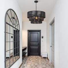 a hallway with a black door, mirror and bench in front of an arched window