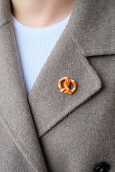 a close up of a person wearing a coat with a pin in the shape of a pretzel