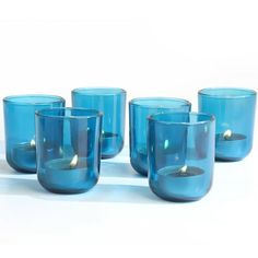 blue glass candlesticks are lined up on a white surface with one lit candle in the middle