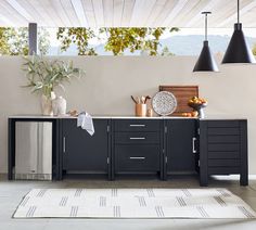 an outdoor kitchen with black cabinets and white rugs on the floor next to it