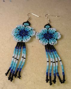 These are hand beaded  huichol style earrings. They are different shades of blue with black accent beads. They are approximately four and a half interest in length.  These can be custom made to any colors preferred. Blue Beaded Dangle Flower Earrings, Bohemian Blue Flower Earrings With Dangling Beads, Blue Flower Earrings With Colorful Beads, Blue Bohemian Flower Earrings, Adjustable Blue Flower Beaded Earrings, Adjustable Flower Shaped Blue Beaded Earrings, Adjustable Blue Earrings With Black Beads, Blue Flower Earrings With Colorful Beads As Gift, Gift Blue Flower Earrings With Colorful Beads