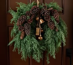 a wreath with pine cones and bells hanging on a door