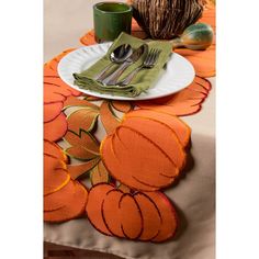 the table is set with an orange and green placemat, silverware, and pumpkins