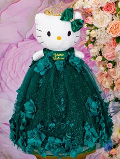 a hello kitty doll dressed up in a green dress with flowers around her neck and wearing a tiara