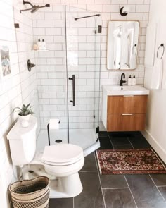 a white toilet sitting in a bathroom next to a sink and shower stall with a rug on the floor