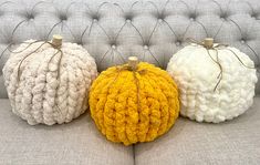 three knitted pumpkins sitting on top of a gray couch next to each other