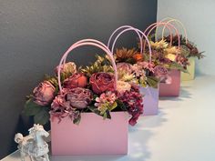 three pink bags with flowers in them sitting on a table next to a small figurine