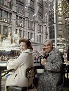 an old man and woman sitting at a table in front of a building