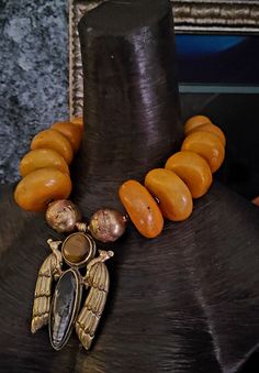 Wow! High End Luxury Ethnic Vibe Statement Necklace Pendant featuring beads ranging in size from 1.5 to 2". Because the beads are handmade, there are imperfections which make them more valuable to collectors. Shown here at a length of 21" but wears more like 19". Closes with gold tone hardware and a fancy lobster claw clasp. If requested, I can add an extender chain free of charge. The 4" x 2.75" pendant features two Tibetan Brass Repousse Peacocks with inlaid Orthoceras Fossil and tigers eye. Two huge Ethiopian hand forged copper beads flank the pendant. Wear alone or layer with coral, turquoise, chrysocolla or warm metals. The perfect statement piece for added drama. Unique Amber Beaded Necklace For Festival, Handmade Artisan Amber Beads, Handmade Artisan Amber Beaded Necklaces, Handmade Artisan Amber Beaded Necklace, Artisan Amber Beads With Large Details, Artisan Large Amber Beads, Unique Pendant With Large Beads, Bohemian Large Gold Beads, Unique Gemstone Beads