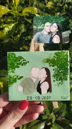 a hand holding up a couple's photo on a matchstick with trees in the background