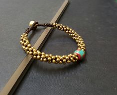 "Single Nepal Handmade Woven Brass Bracelet M a t e r i a l : ♡ brass bead ♡ bell ♡ nepal bead ♡ wax cord S i z e : 7.5\" S h i p p i n g : ♡ All items shipped worldwide by Thailand post. ♡ Shipped within 2- 3 days after payment received. ♡ Can be upgrade to express mail by a request before payment. You will take : ♡ 15 - 25 days after shipped from Thailand . ♡ 5- 7 days after shipped from Thailand by express mail." Hand-strung Brass Bracelets With Round Beads, Brass Bracelets With Round Gold Beads, Brass Beaded Bracelets With Round Beads, Adjustable Beaded Bracelets For Rituals, Adjustable Gold Bead Brass Bracelets, Adjustable Polished Beads Bracelets For Festivals, Spiritual Beaded Brass Bracelets, Spiritual Brass Beaded Bracelets, Gold Hand-strung Braided Bracelet For Festivals