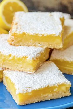 several lemon bars stacked on top of each other with powdered sugar and two lemons in the background