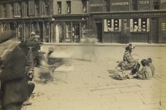 an old black and white photo of people sitting on the ground in front of buildings