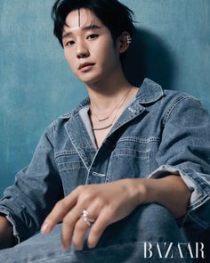 a young man sitting on top of a blue wall wearing a ring and jeans jacket