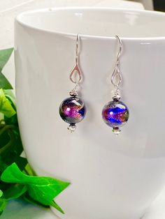 "Bold and dynamic colors swirl and sparkle against a black background in these dichroic glass earrings! Sterling silver foil is encased in each bead to accentuate the brilliant colors of pink, blue and silver. The Venetian Murano beads are 12mm rounds. Faceted silver Hematite rondelle beads accent the glass beads for added sparkle and shine. The earrings hang 1.5 inches on Sterling silver ear wires with a teardrop loop. A wonderful gift for any occasion and arrives in a standard gift box. FOR GI Murano Glass Earrings, Dichroic Glass Earrings, Jewelry Colorful, Murano Glass Jewelry, Color Swirl, Colorful Jewelry, Dichroic Glass, Silver Foil, Glass Earrings