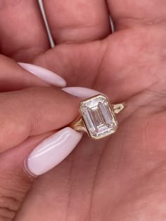 a woman's hand holding a ring with an emerald stone on it and white acrylic nails