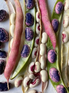 beans and pea pods are laid out on a white surface with purple speckles