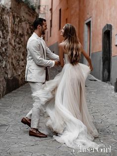 a bride and groom walking down an alleyway in the middle of town holding hands