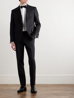 a man in a tuxedo standing on a wooden floor with his hands in his pockets