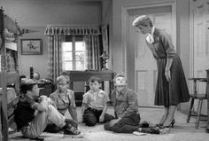 a group of children sitting on the floor in front of a woman standing over them