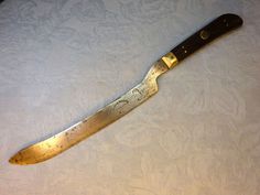 a large knife sitting on top of a white tablecloth covered surface with an intricate design