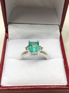 Displayed is a classic Colombian emerald three stone emerald-cut engagement ring in .925 sterling silver. This gorgeous ring carries a full 2.0-carat emerald in a four prong setting. Fully faceted, this gemstone showcases excellent shine. The emerald has excellent clarity with minor flaws that are normal in all genuine emeralds but no carbon spots (black) or harsh flaws are found in this beauty! The gem has a light green color and excellent luster. Two natural diamonds accent the emerald. An ide Radiant Cut Three Stone Ring Gift, Three Stone Radiant Cut Ring For Gift, Green Three Stone Emerald Cut Jewelry, Radiant Cut Three Stone Ring As A Gift, Fine Jewelry Radiant Cut Emerald Anniversary Ring, Fine Jewelry Radiant Cut Emerald Ring With Accent Stones, Gift Emerald Ring With Three Stones In Radiant Cut, Formal Three-stone Emerald-cut Birthstone Ring, Silver Emerald Cut Ring For May Birthstone