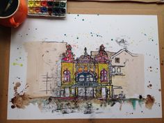 a drawing of a building on paper next to a cup of coffee and paintbrushes