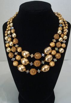 This is a beautiful three strand gold bead necklace by Lisner.  It is comprised of shiny gold beads, filigree gold beads, and textured gold beads. The large oval shiny gold beads are 19mm.  The filigree beads range from 14mm down to 9mm. Smaller textured and shiny beads complete the necklace.  In addition there are clear crystal AB pinched bicone beads and gold connector beads. The J-hook is signed Lisner. The wearable maximum length is 18 inches.  The necklace is in excellent vintage condition and would be perfect for the holidays.  Lots of sparkle. Sugar Beads, Glass Ball Ornaments, Gold Bead Necklace, Crystal Ab, Copper Pendants, Gold Texture, Gold Beads, Purple Gold, Chain Styles