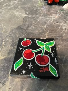 a black box with red cherries on it sitting on a marble table next to some candy