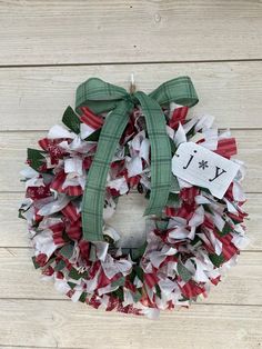 a red and white christmas wreath with a green bow on the front hanging on a wooden wall