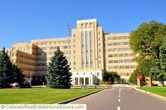 the large building has many windows and trees on it's sides, along with an empty street in front