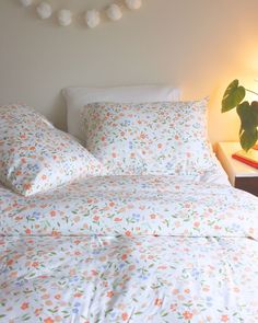 a bed with white and orange flowers on it, next to a night stand with a lamp