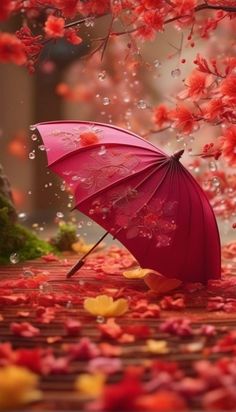 an open umbrella sitting on the ground in front of red leaves and trees with pink flowers