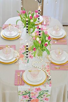 the table is set with pink and white flowers in vases, plates, napkins, and goldware