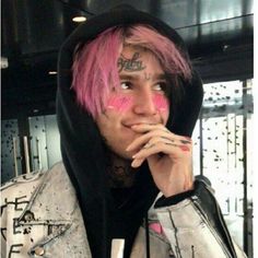 a man with pink hair wearing a white jacket and black hoodie is holding his hand to his mouth