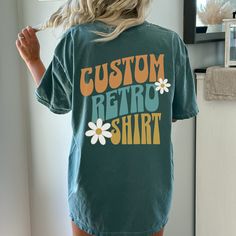 Show off your retro style with this Custom 3 Word Retro Font Oversized T-shirt. The vintage font is sure to make a statement and bring you back to the fun, classic days of the past. And the added flowers give you a groovy vibe. With roomy, oversized fit, you'll be able to express yourself with comfort and ease. Ideal for any casual occasion, this T-shirt's retro look will take your wardrobe to the next level. This custom design T-shirt comes in your choice of 12 vibrant colors, perfect for makin Retro Cotton Shirt With Letter Print, Vintage Short Sleeve T-shirt With Lettering, Retro Graphic Print Crew Neck Top, Retro Crew Neck Top With Graphic Print, Vintage Crew Neck Shirt With Graphic Print, Retro Green Top With Letter Print, Retro Green Top With Screen Print, Vintage Oversized Crew Neck T-shirt, Retro Green Screen Print Top