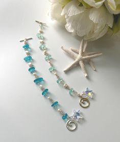 two necklaces are laying next to a starfish on a white surface with flowers in the background