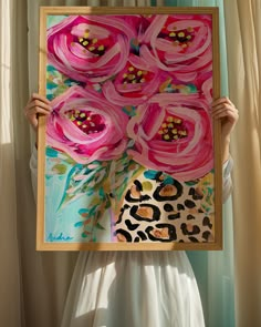 a woman holding up a painting with pink flowers