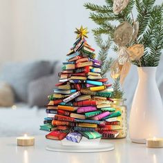 a christmas tree made out of books sitting on a table next to a vase filled with candles