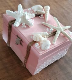 a pink box with seashells and starfish on the top is sitting on a wooden table