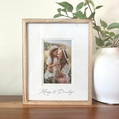 a white vase sitting on top of a wooden table next to a framed photo and a plant