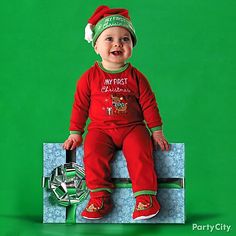 a baby sitting on top of a green bench wearing a santa hat and red pajamas