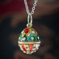 "This fabulous vintage egg pendant is beautifully decorated with twinkling white pastes, a cabochon garnet on the bottom and teardrop and leaf motifs, highlighted in bright red and green guilloche enamel.  Guilloche enamel dates to the 17th century and involves metal carefully worked by a lathe, or \"Rose Machine\" into a decorative pattern and overlaid with a colourful enamel to create a striking and highly detailed work of art.  It's a beautiful design, similar to that of a Faberge egg and is modelled in gold metal and is accompanied by a sterling silver cable chain to display it on.  WEIGHT: Egg 9.7 grams - Chain 3.6 grams   MEASURES: Egg Height 20mm (30mm inc. loop) x Width 16mm x Depth 16mm - Chain Length 18 inches x Width 1.5mm  METAL: Base Metal/ Sterling Silver chain STONES: Glass Oval Enamel Locket Jewelry, Oval Enamel Locket Necklace, Oval Locket Necklace In Enamel, Antique Enamel Jewelry As Gift, Antique Enamel Jewelry For Gift, Antique Enamel Jewelry As A Gift, Formal Jeweled Enamel Jewelry, Ornate Red Cabochon Jewelry, Ornate Red Teardrop Jewelry