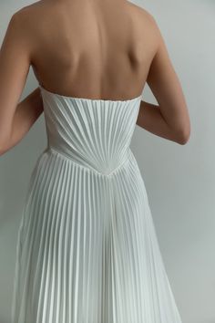 the back of a woman's white dress with pleated skirt and high heels