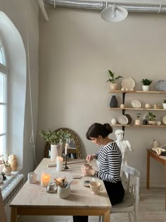 a woman sitting at a table in front of a window with candles and dishes on it