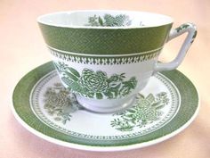 a green and white tea cup with matching saucer on a pink cloth tablecloth