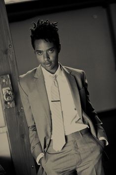 a man wearing a suit and tie standing next to a wooden door with his hands in his pockets