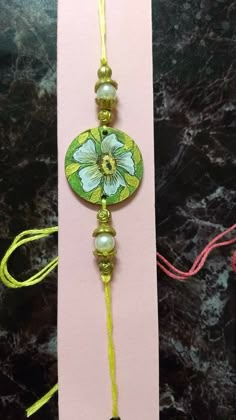 a green and white flower beaded necklace on a pink card with yellow string attached to it