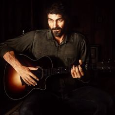 a man sitting in the dark holding a guitar and looking at the camera with one hand